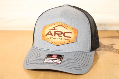 Gray and black cap with ARC Installation leather patch on a wooden surface