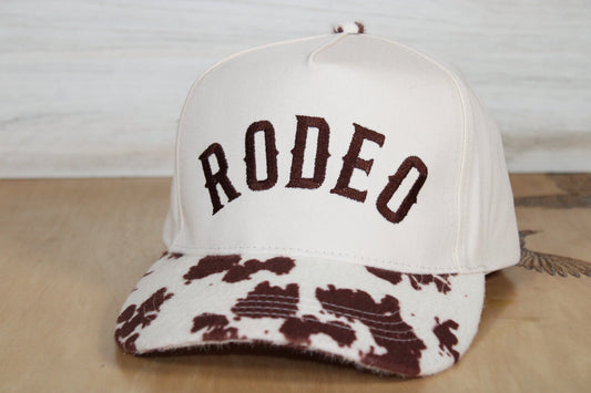 White cap with brown cow print and 'RODEO' text on a wooden surface.