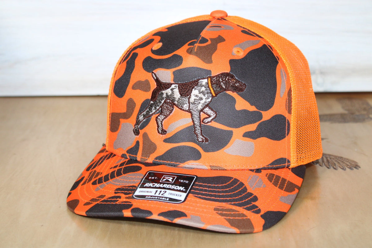 Orange and black camouflage cap with a dog graphic on a wooden surface