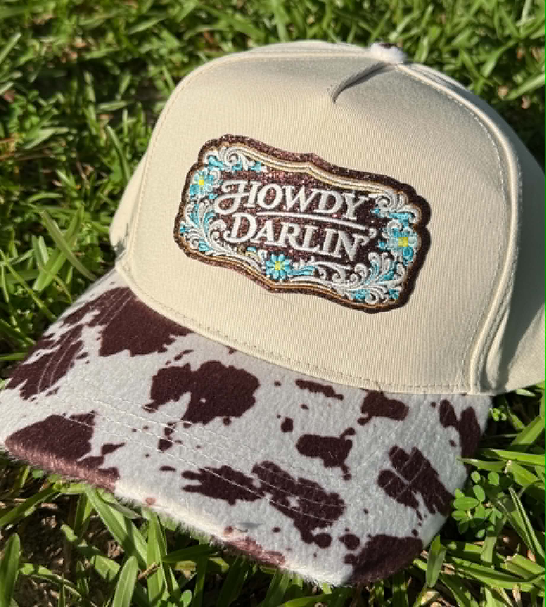 Cap with 'Howdy Darlin' logo on a grass background