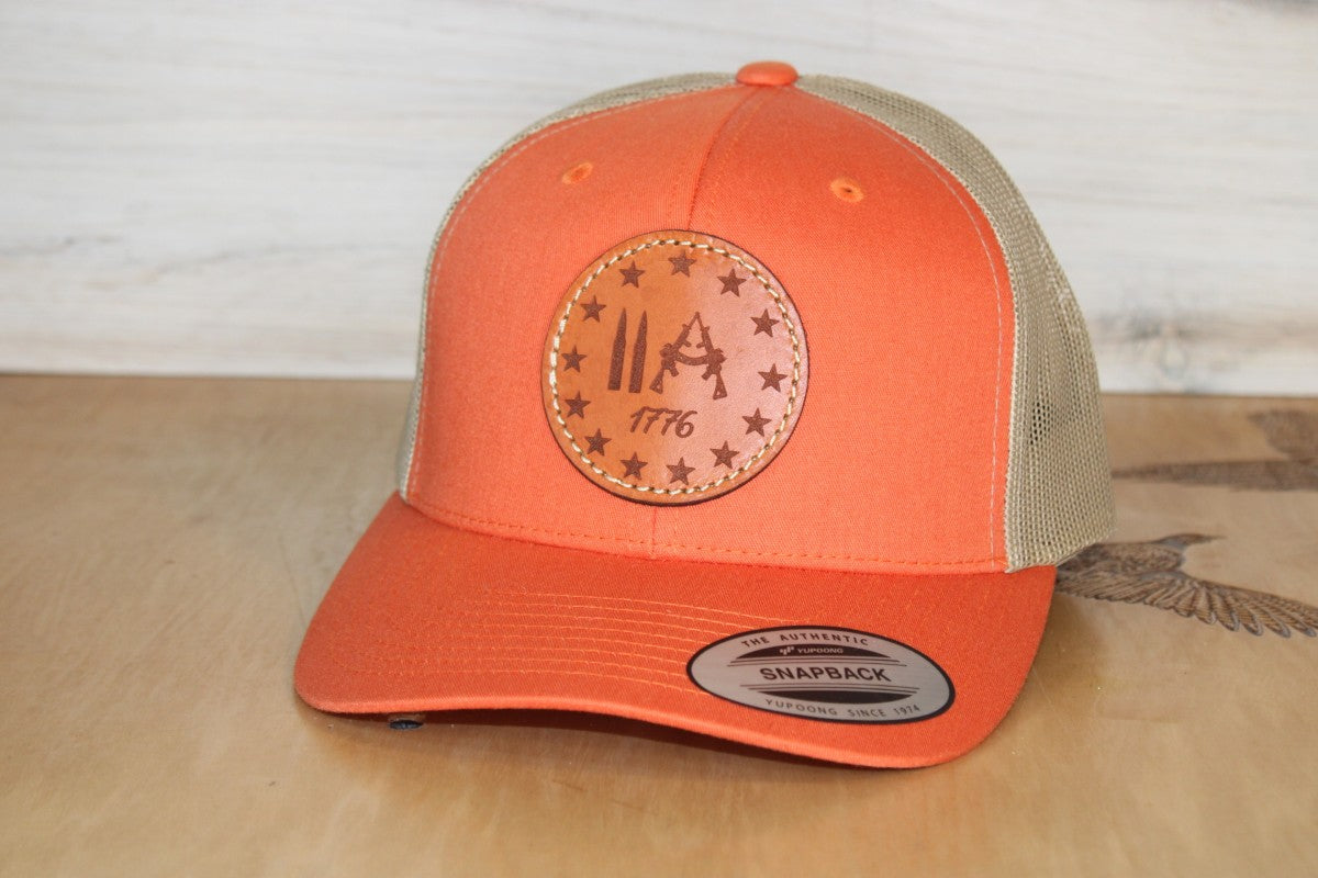 Orange and beige cap with a try that in a small town leather patch