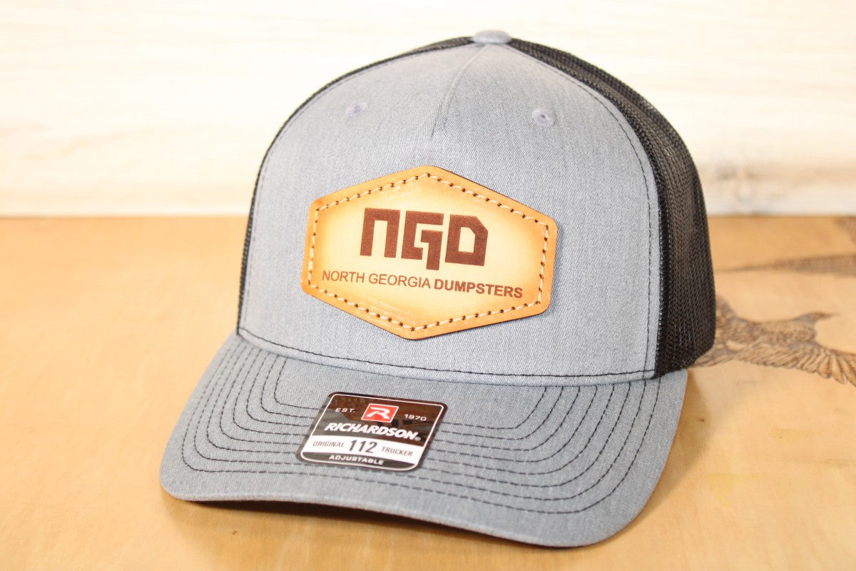 Gray and black cap with a North Georgia Dumpsters leather patch on a wooden surface