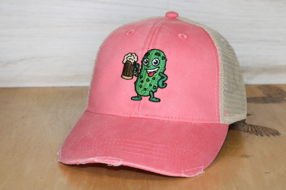 Pink cap with a cartoon pickle holding a beer on a wooden surface