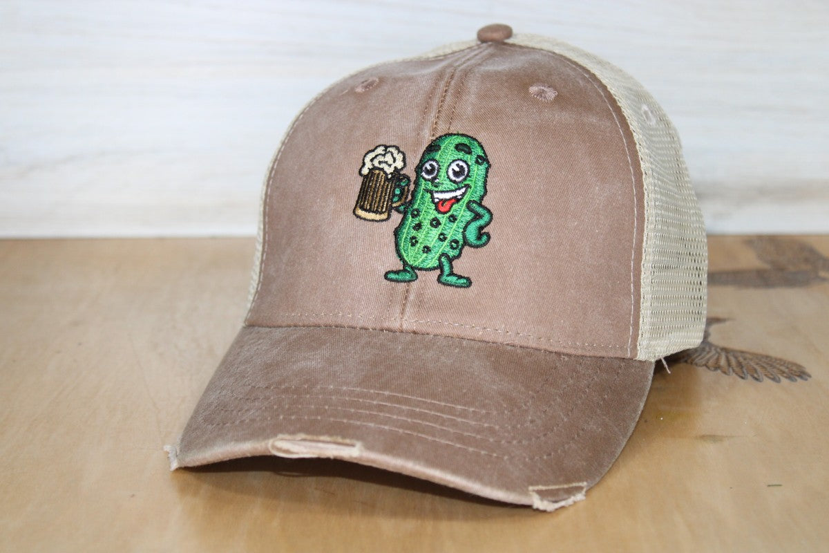 Brown trucker cap with a pickle holding a beer on a wooden surface