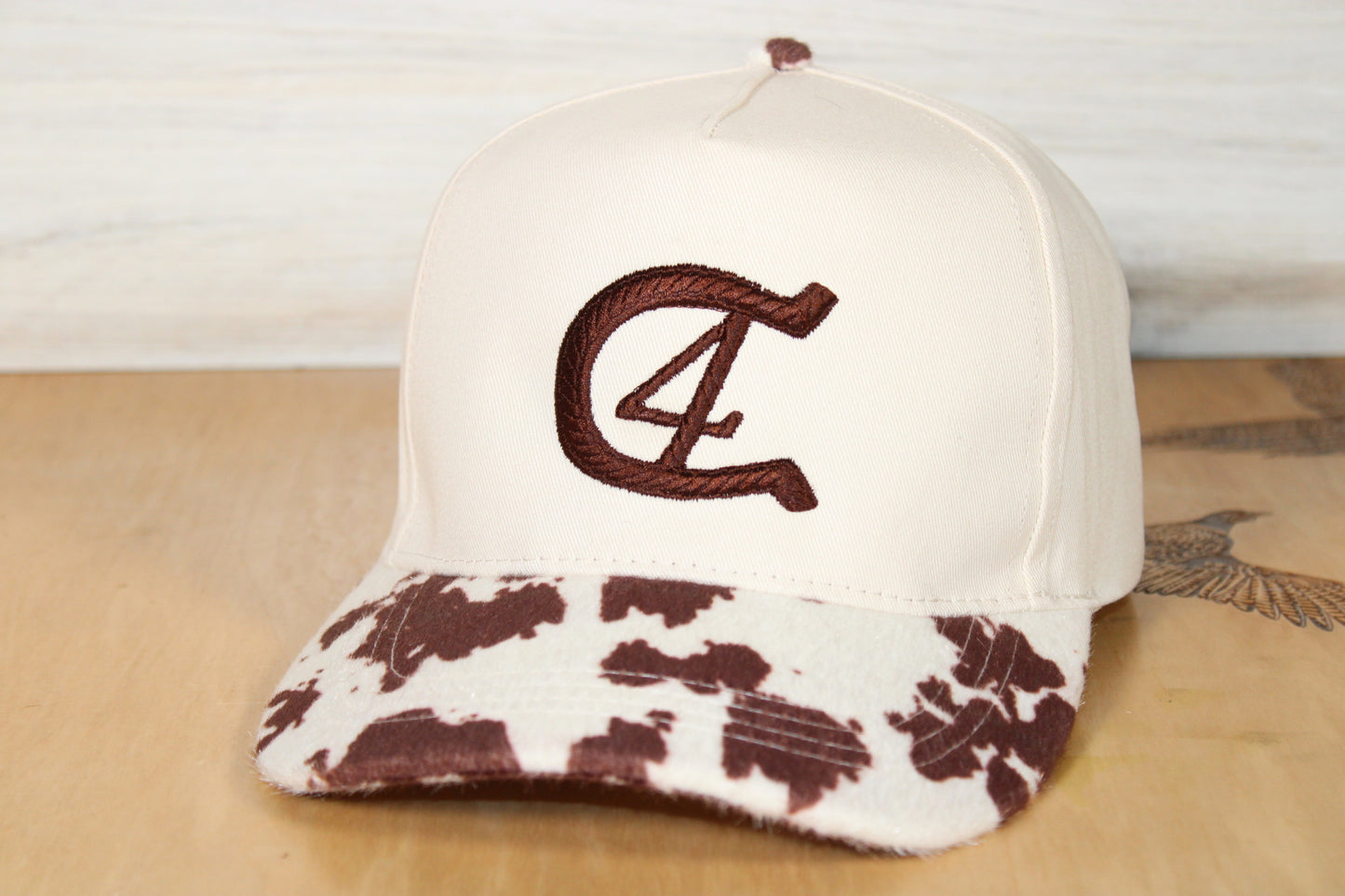 White cap with brown patterned brim and horse shoe logo on a wooden surface